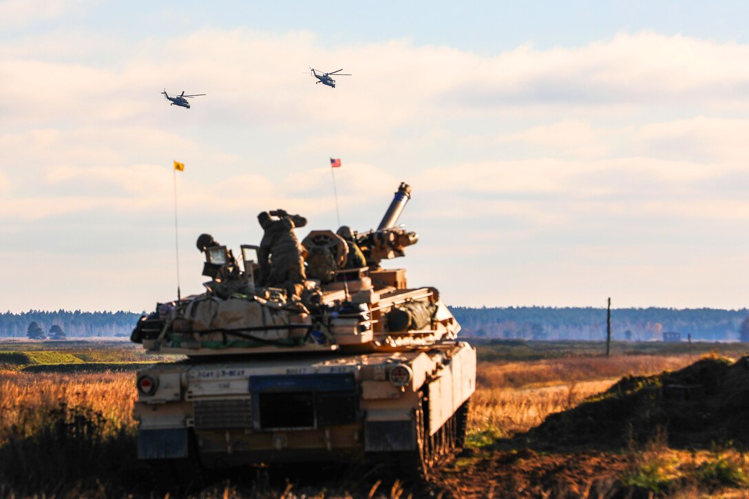 Soldiers watch two helicopters fly above them.