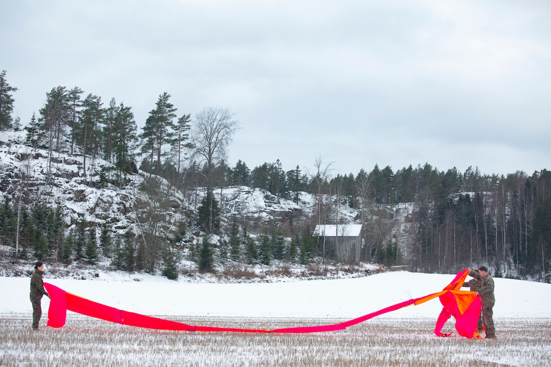 Marines unfold a large pink material in a snowy field.
