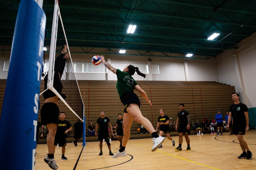 A soldier spikes a volleyball above the net during a  game.