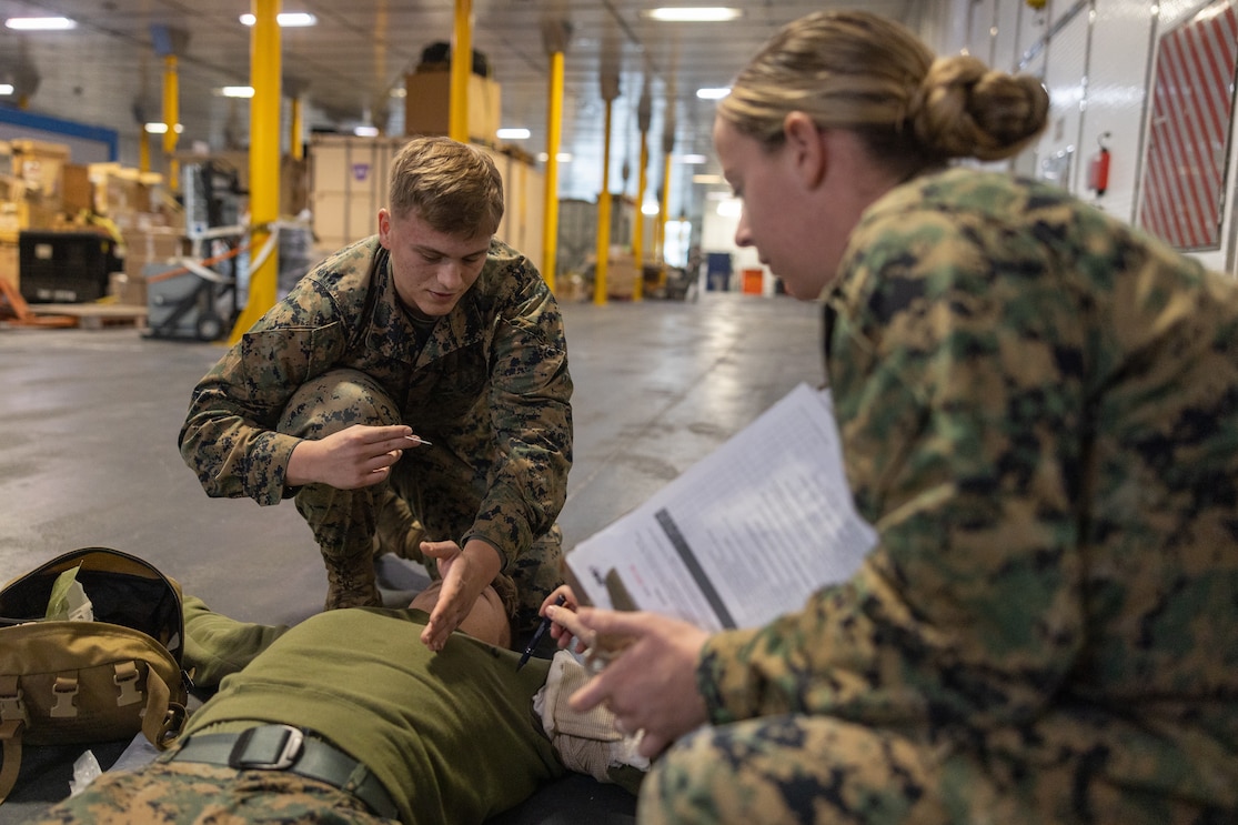 U.S. Marine Corps Cpl. Patrick Maddox, left, an ammunition technician, from Muhlenberg, Kentucky, explains to U.S. Navy Hospital Corpsman 3rd Class Lynsey Harris, right, from Lawrence, Kansas, both assigned to 8th Engineer Support Battalion, 2nd Marine Logistics Group, II Marine Expeditionary Force (MEF), the process of inserting a needle decompression during a tactical combat causality care practical application evaluation aboard the Spearhead-class expeditionary fast transport ship USNS Trenton (T-EPF 5) in Greece, November 28, 2022.