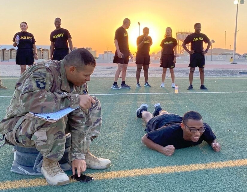 A group of service members work out in a field while the sun sits just over the horizon.