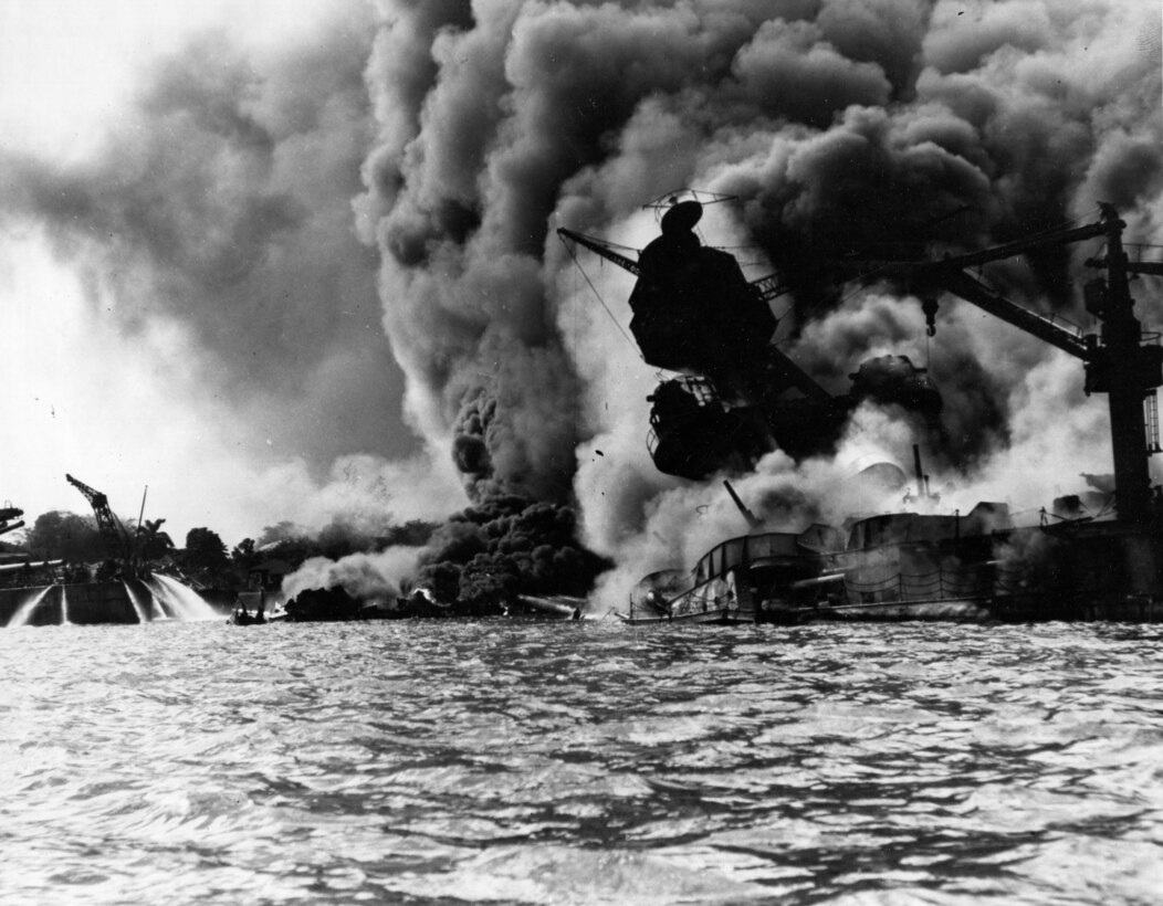 Massive plumes of smoke rise from a sinking ship. A nearby ship sprays water out of hoses.