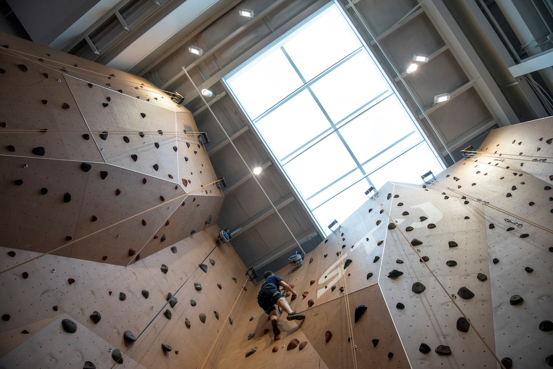 An RSM is seen from below as he make his way up a climbing wall towards a skylight.