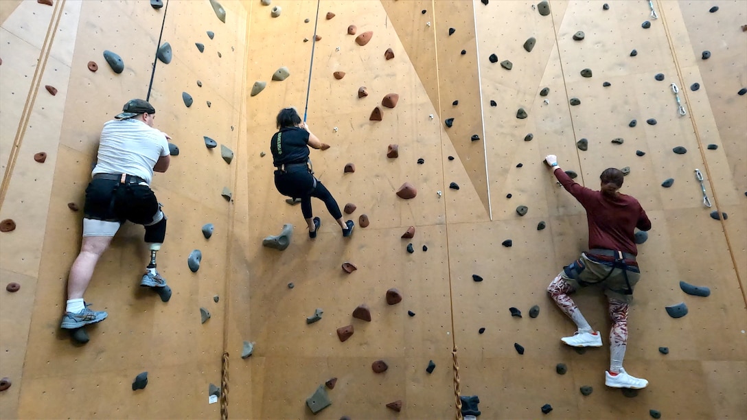 Three RSMs scale a climbing wall.