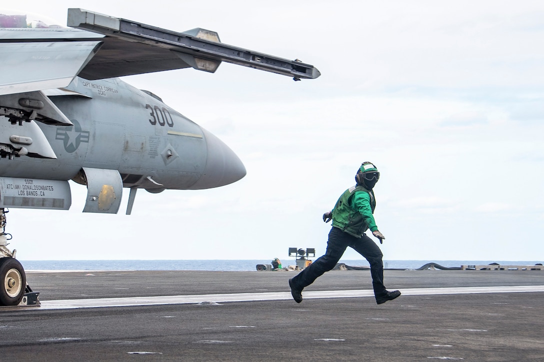 A sailor runs next to an aircraft aboard a ship at sea.