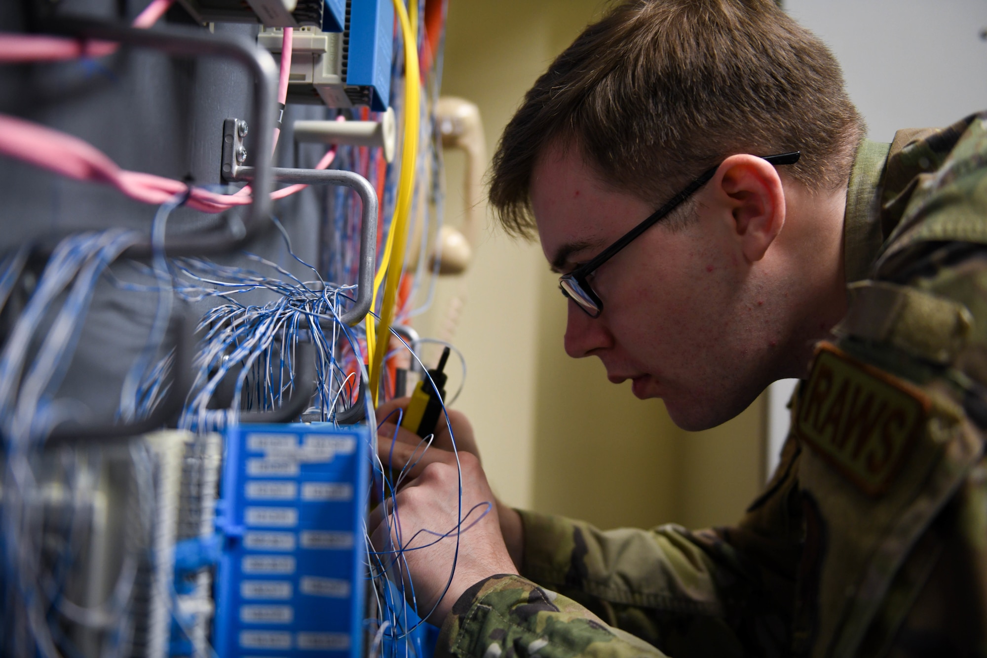 An airman with glasses connects wires.