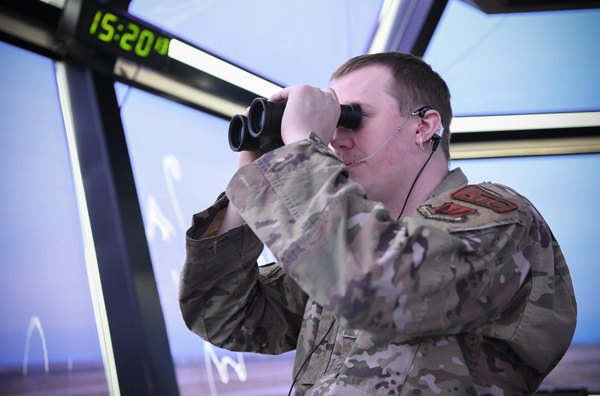 A man in a green uniform looks through binoculars.