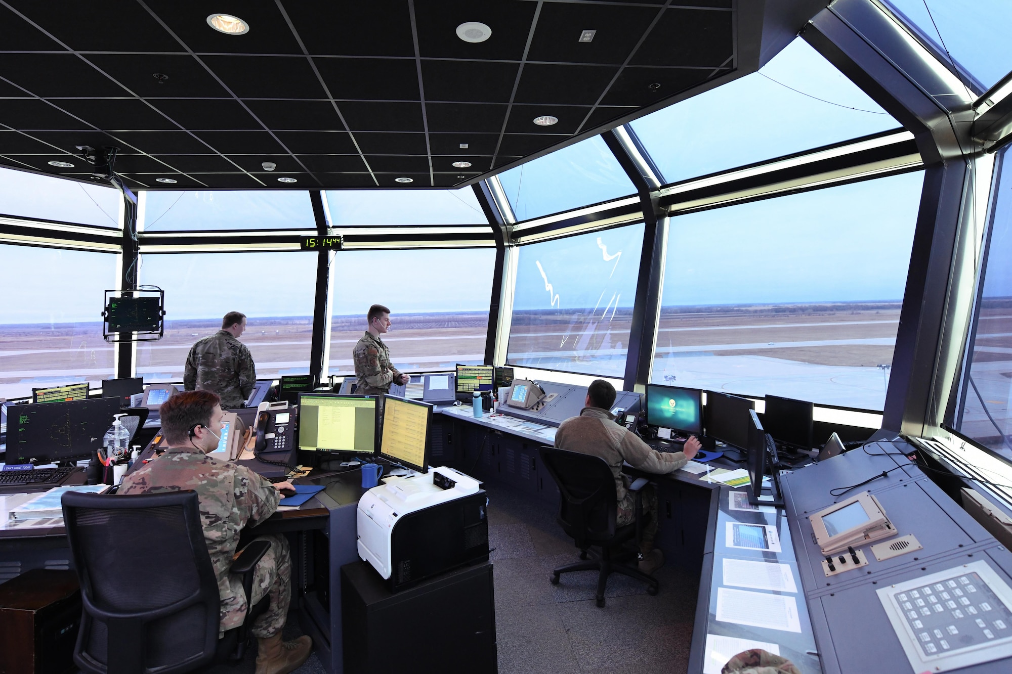 Four airman sit inside a air traffic control tower looking out.