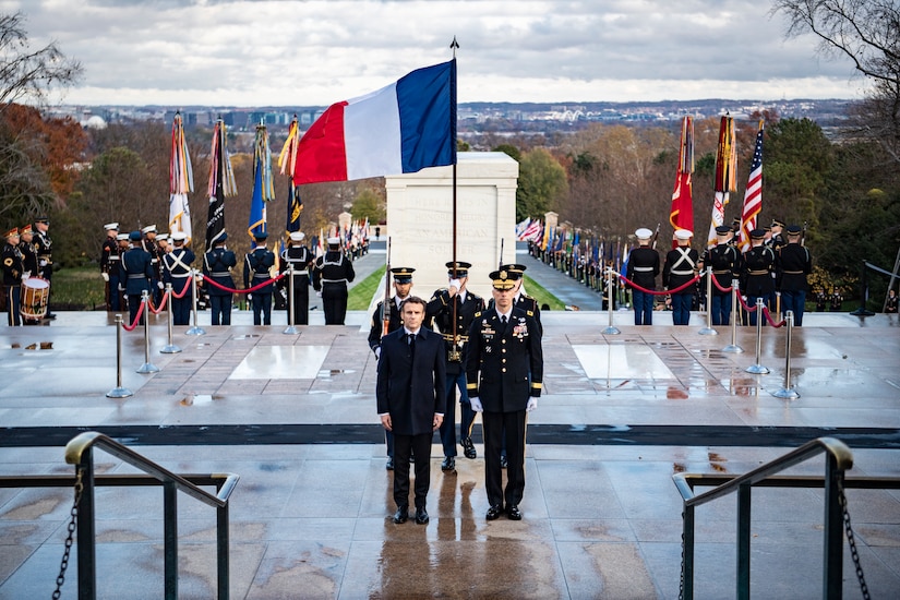 Two men stand in front of three service members; behind the group is a monument.