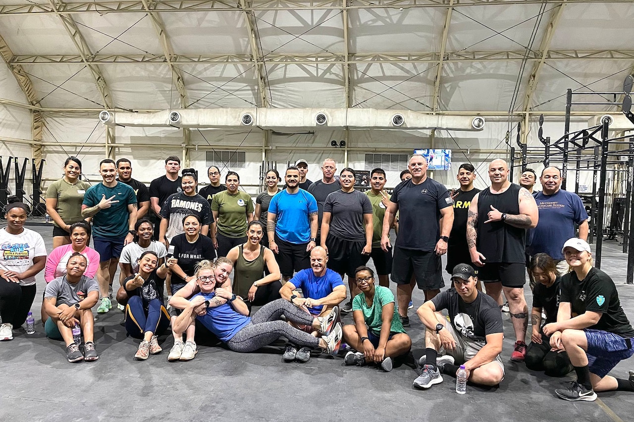 A group of people pose for a photo in a large tent full of fitness equipment.