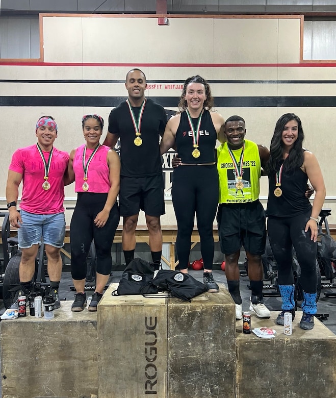 Six people wearing medals around their neck stand on wood boxes and pose for a photo.