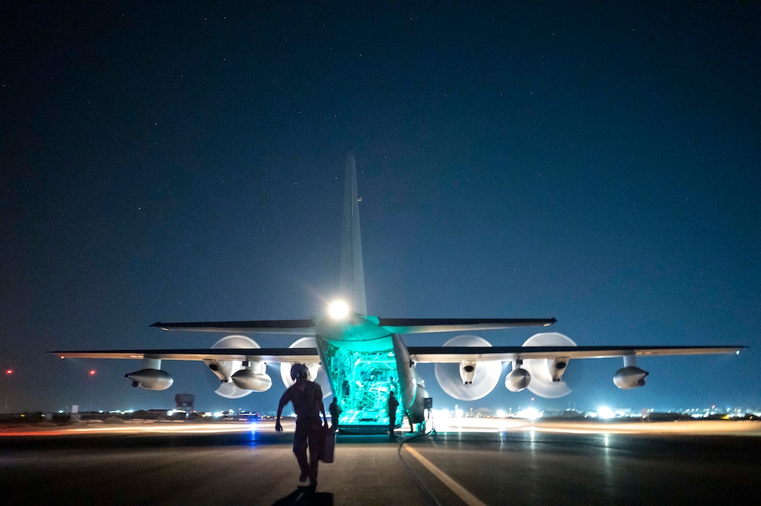 An airman walks away from an aircraft at night while two people stand at the back of the plane’s open cargo bay.