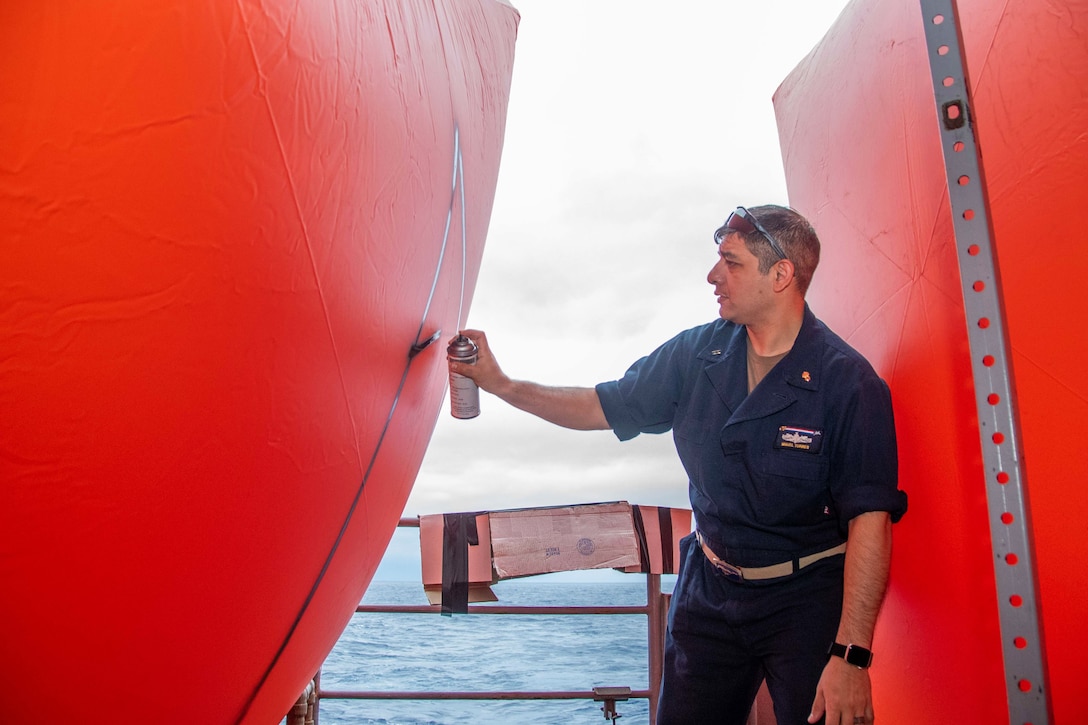 A sailor sprays a mark onto a large inflated orange buoy.