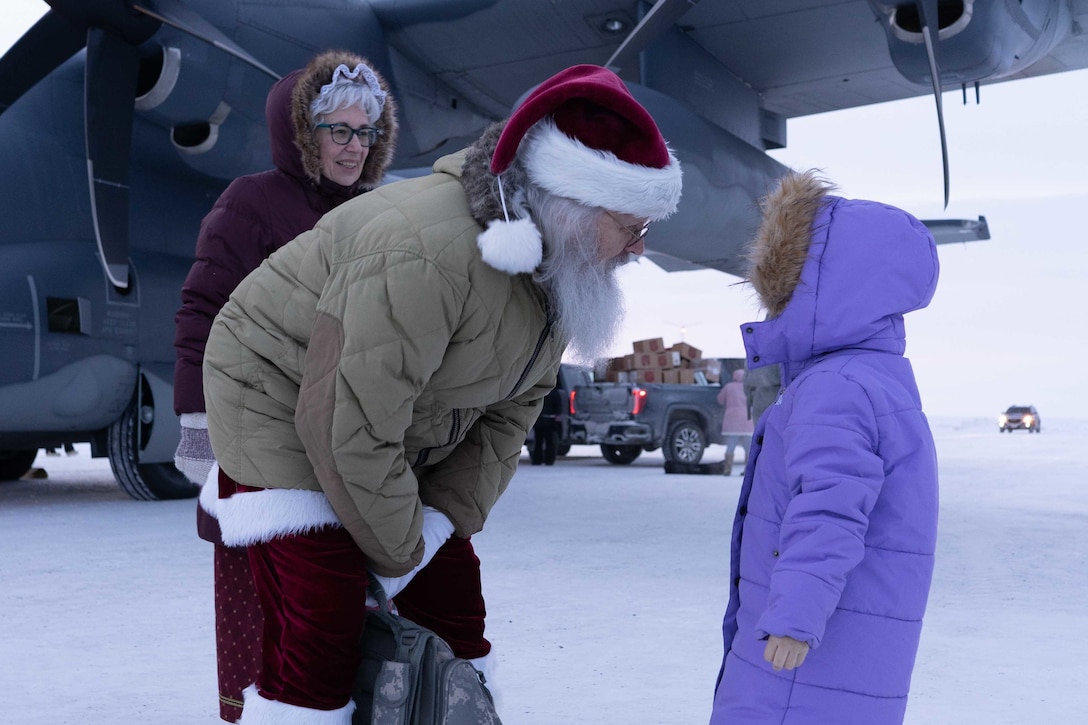 Santa and Mrs. Claus greet a child at the Nuiqsut airport as part of Operation Santa Claus Nov. 29, 2022. The Clauses and more than three dozen elves from the Alaska Air and Army National Guard partnered with the Salvation Army to deliver 1,420 pounds of gifts, hygiene supplies, and books to 191 children. Celebrating 67 years of Operation Santa Claus, a 176th Wing, Alaska Air National Guard HC-130J Combat King II aircraft served as Santa's sleigh, delivering tidings of good cheer to the North Slope Borough community