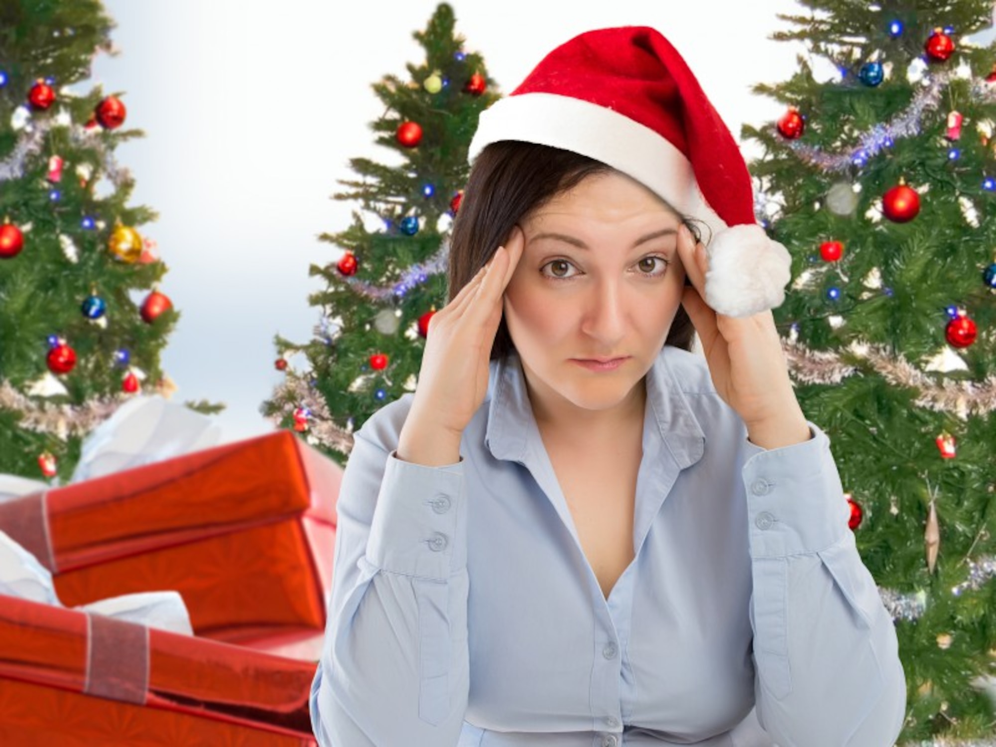 A woman wearing a Santa hat holds her head as if she's stressed.