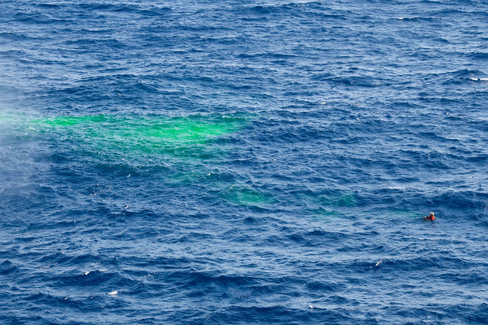 A diver floats in a sea next to dye waiting for rescue