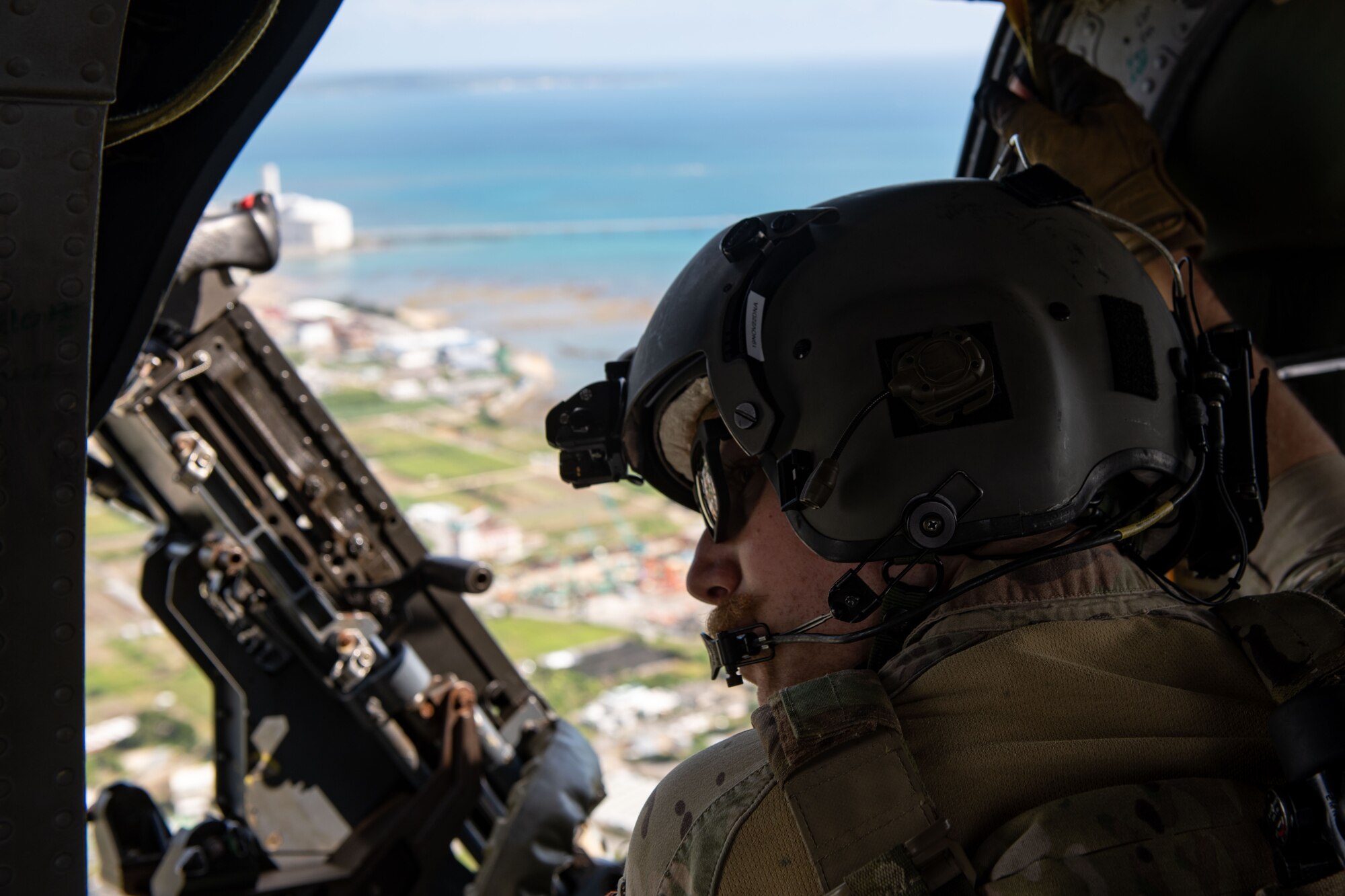 A helicopter crew member looks out the door of a helicopter