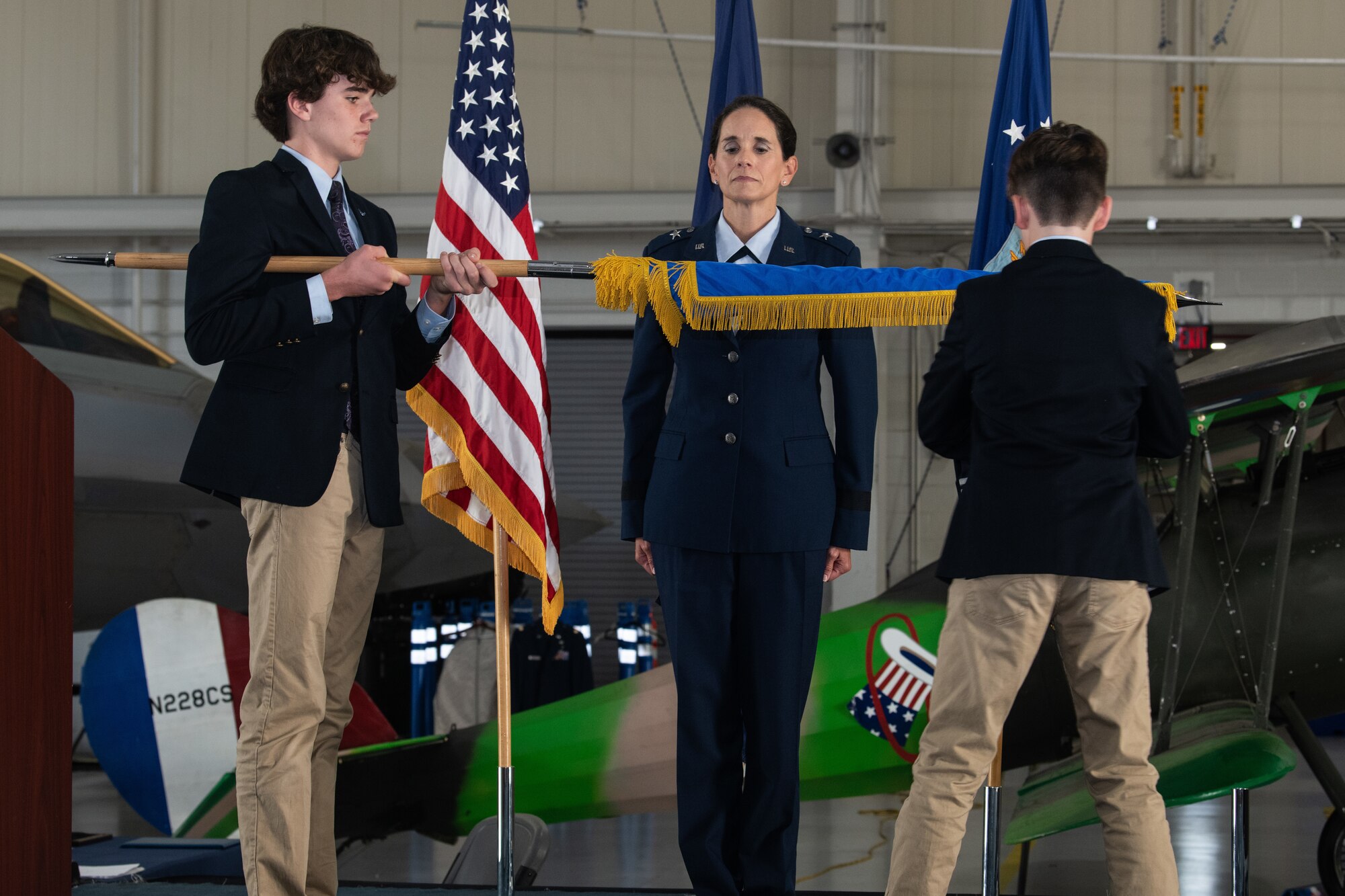 Brig. Gen. Catherine M. Jumper is standing on stage while her sons unfurl her official one star general flag.