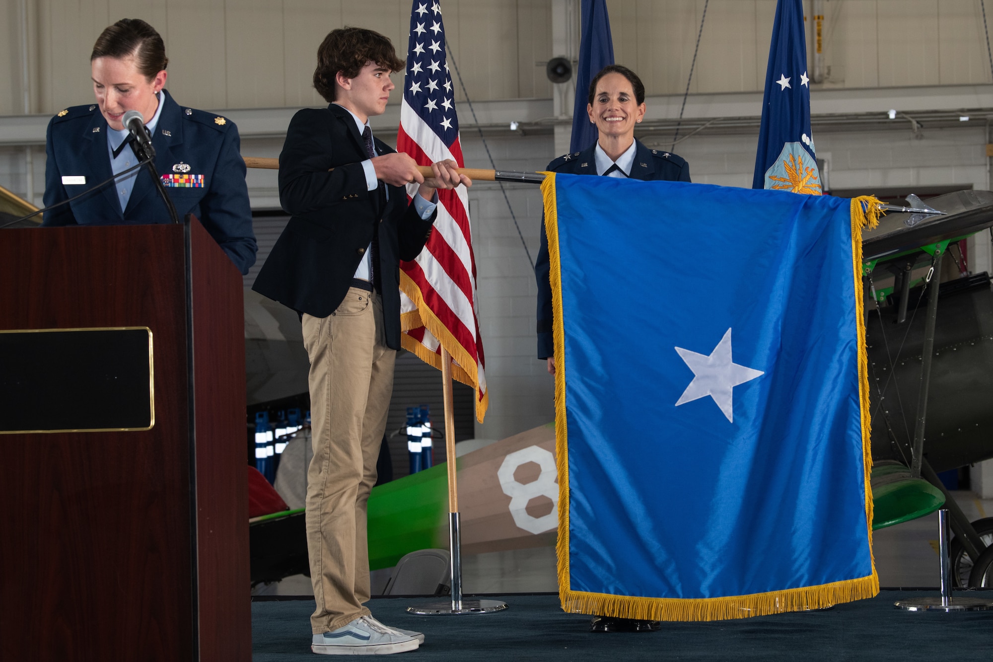 Brig. Gen. Catherine M. Jumper is standing on stage while her oldest son unfurls her official one star general flag.
