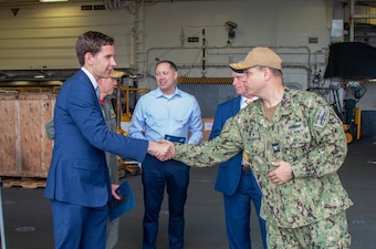 Captain in uniform shaking hands with another man in blue suits with few people behind them on the ship.