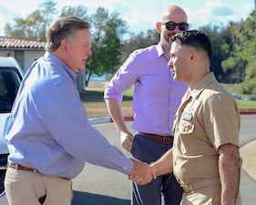 Two men shaking hands on sunny day with a person behind them. Capt Mike Aiena on right shaking hands with U.S. Rep Ken Calvert