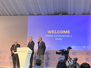 Men in suits at podium speaking to the audience with powerpoint projected behind them.