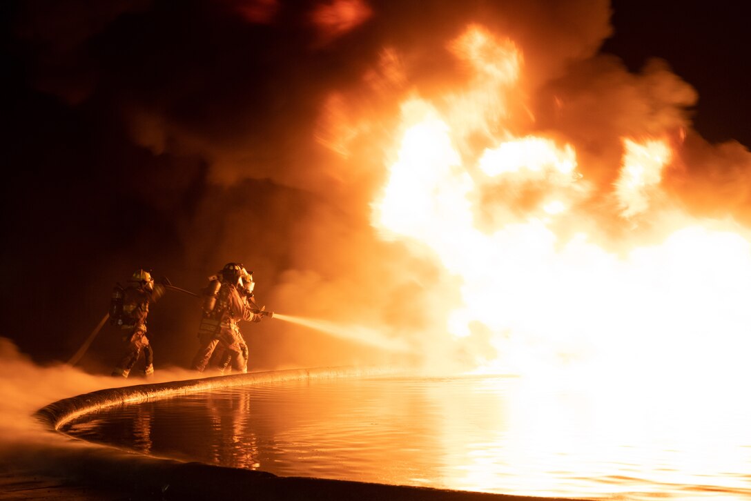 Marines man a hose while spraying a giant fire.