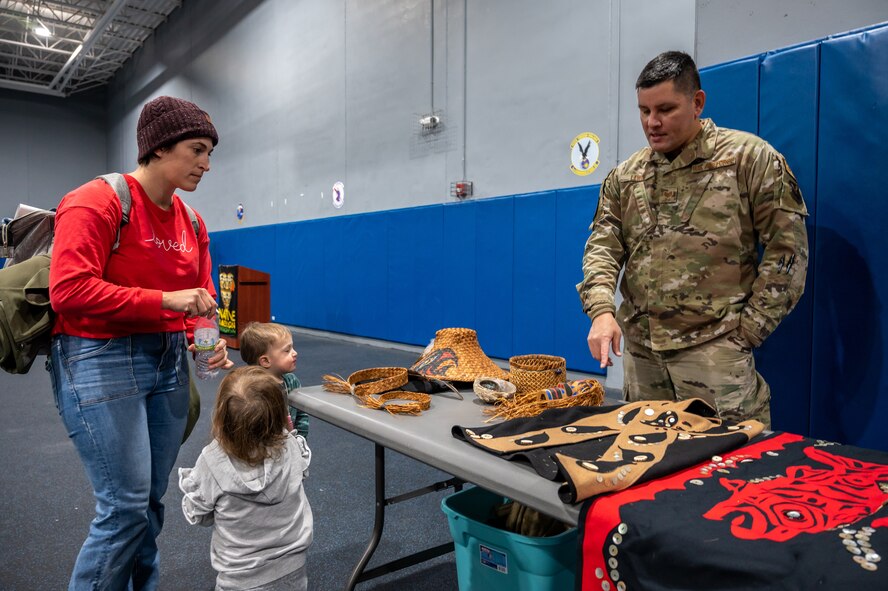 Tech Sgt Pashala Lewis, a Native American Airman, explains his family’s traditions to a mother and children at Minot Air Force Base, North Dakota, Nov. 30, 2022. During the ceremony, attendees learned about Native American culture from local tribes and Native American Airmen. (U.S. Air Force photo by Airman 1st Class Alexander Nottingham)