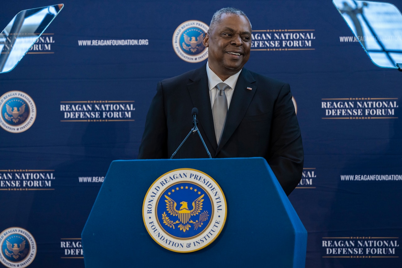 Secretary of Defense Lloyd J. Austin III smiles from behind a lectern.