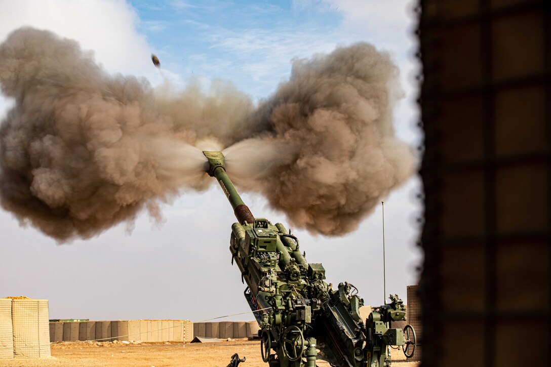 A round fires and huge plumes of smoke spill from both sides of an M777 Howitzer.