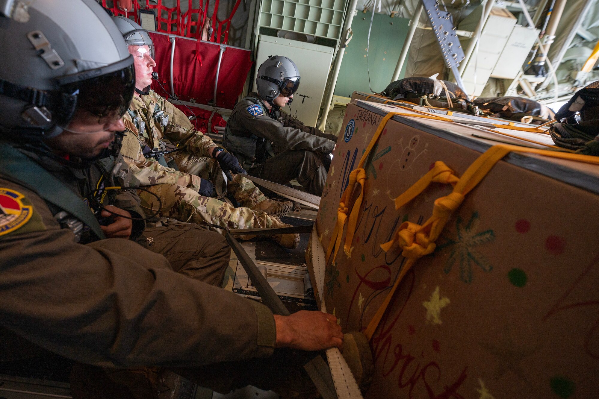 Airmen sitting in the cargo bay of a C-130 prepare to push bundles out of the aircraft