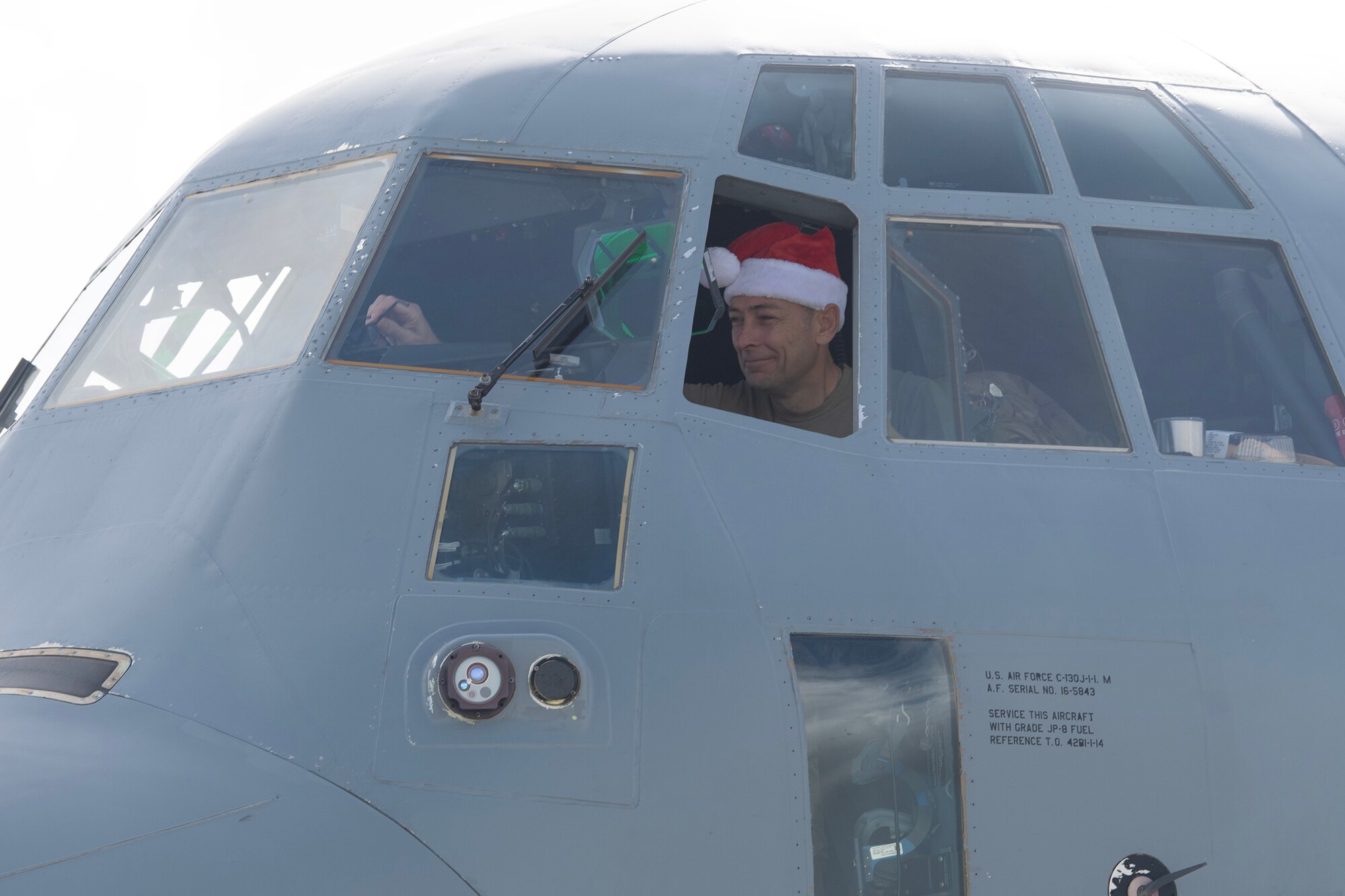 A man with a santa hat is sitting in the cockpit of a C-130J Super Hercules aircraft