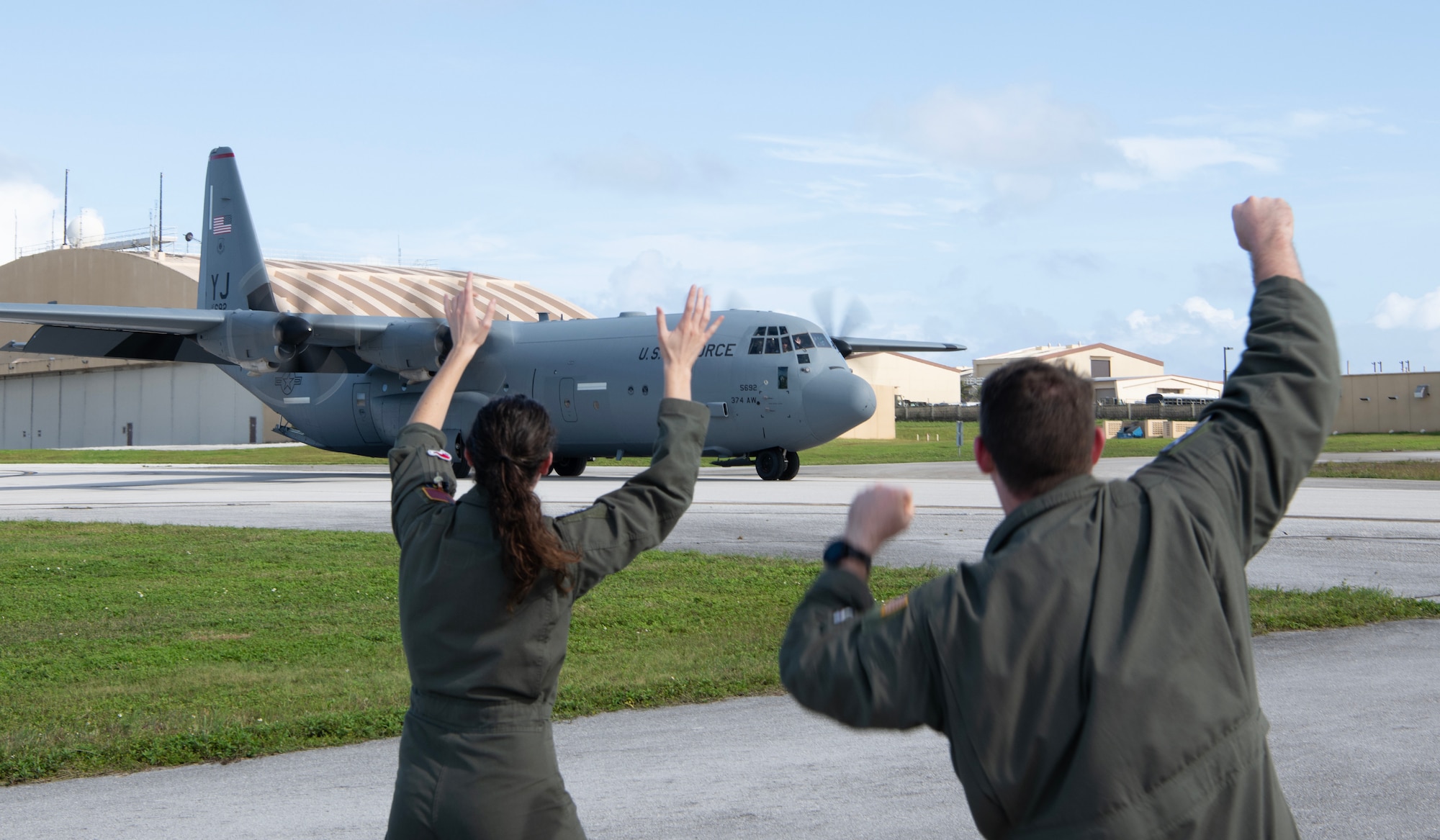 two people waving at a C-130J as it arrives to Andersen Air Force Base.