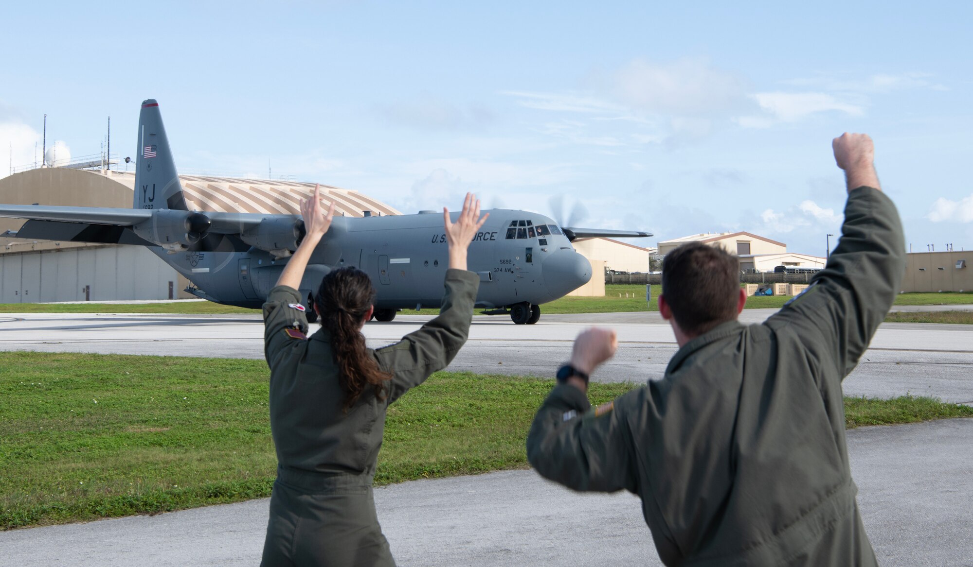 two people waving at a C-130J as it arrives to Andersen Air Force Base.