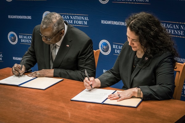 Secretary of Defense Lloyd J. Austin III and the SBA administrator sign documents at a table.
