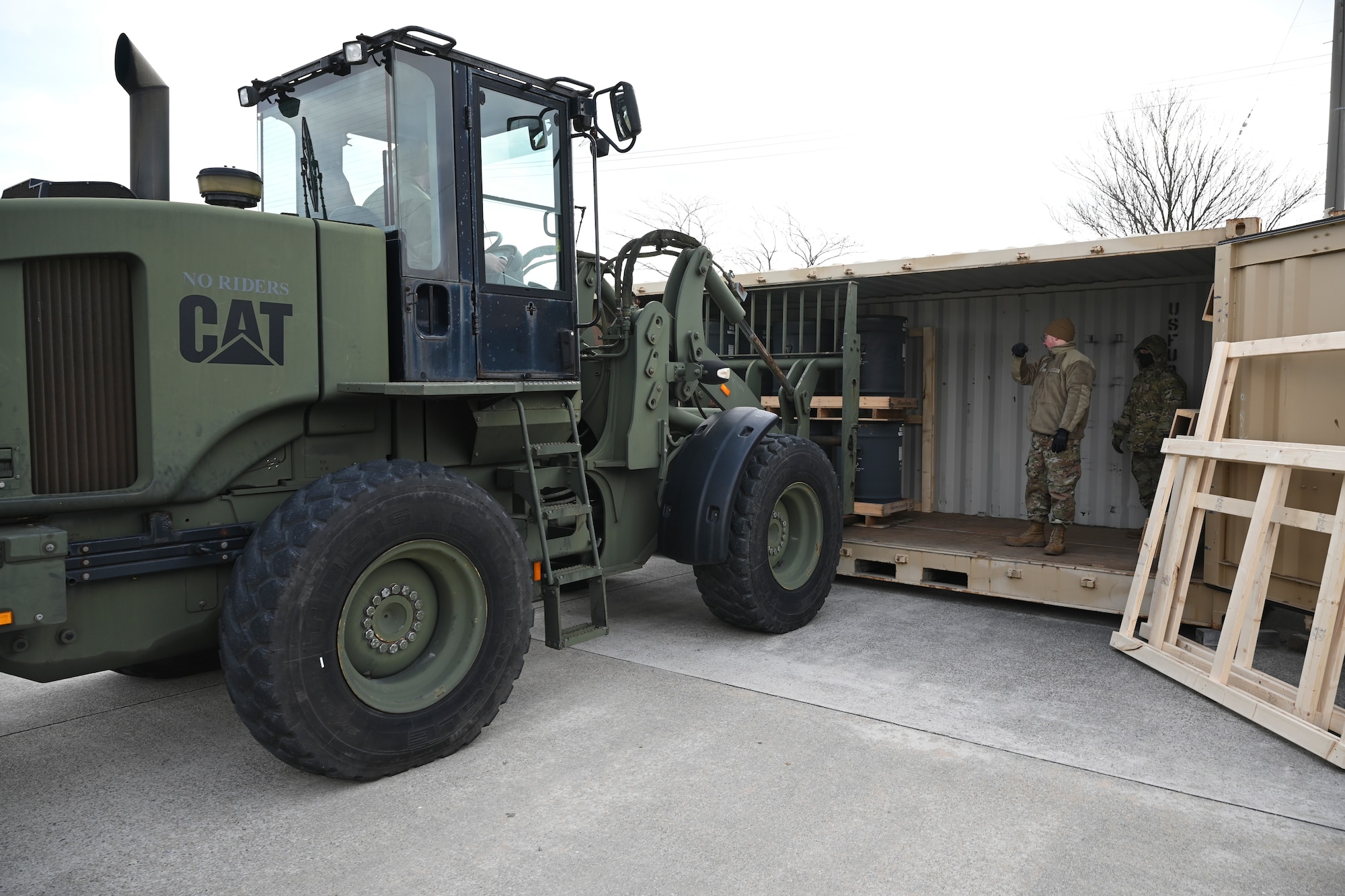An Airman directs another Airman in a large forklift on how to place the munition in the intermodal shipping container.