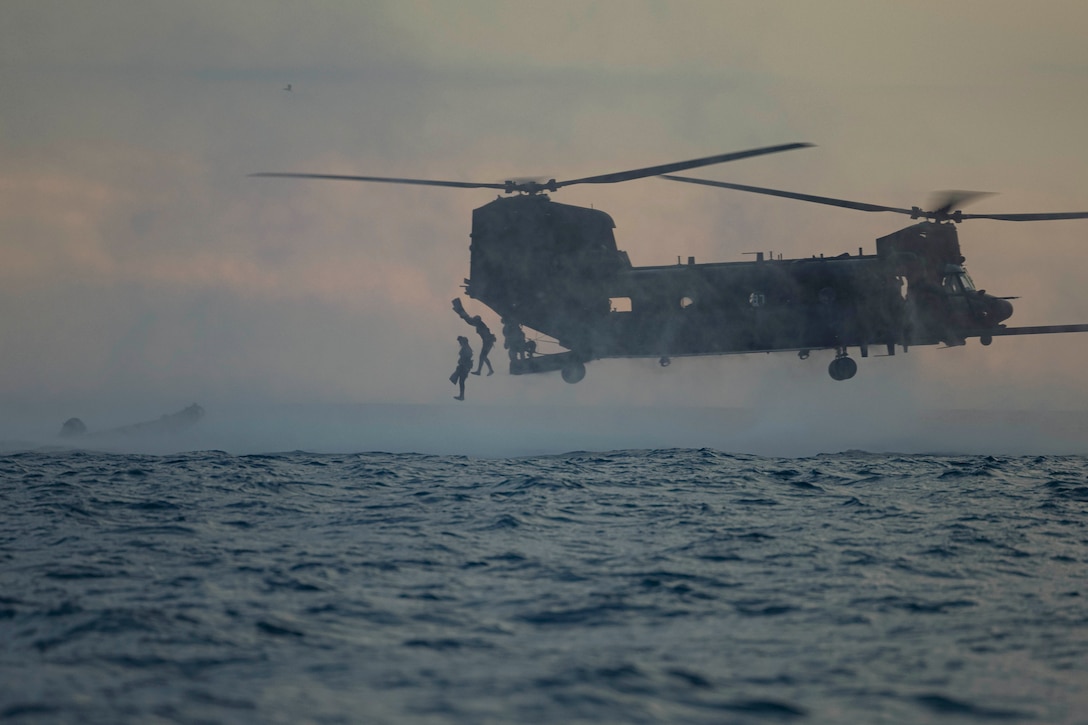 Two Marines jump out of an Army helicopter into a body of water.