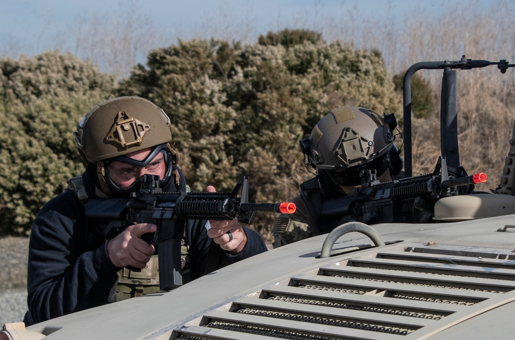 Airmen take cover behind a vehicle.