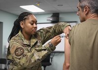 A female airman gives a male airman a flu shot during a medical readiness event.