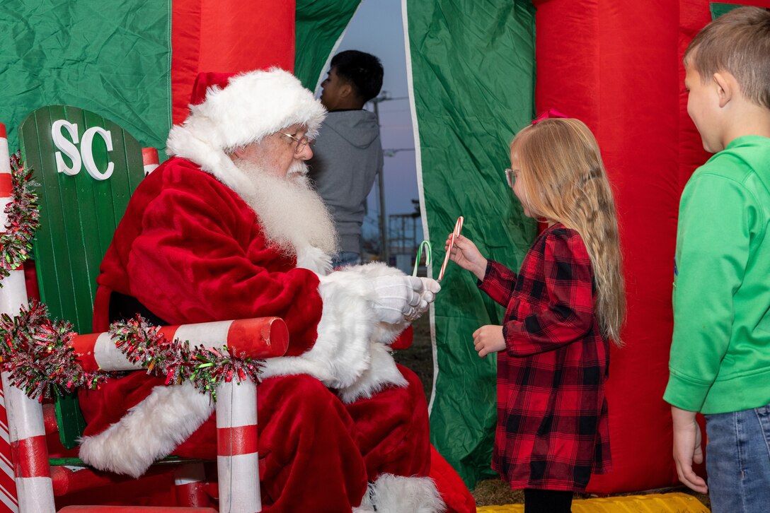 Santa Claus hands a candy cane to a young girl during the annual Christmas Tree Lighting Ceremony on Marine Corps Air Station Cherry Point, North Carolina, Dec. 1, 2022. The event featured several live performances, a holiday selfie station, a Letters to Santa station, a Santa Claus meet and greet, and free cookies and hot cocoa. (U.S. Marine Corps photo by Lance Cpl. Matthew Williams)