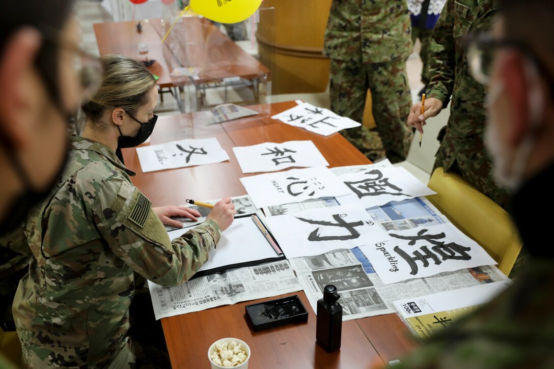 A soldier writes large Japanese characters as others watch.