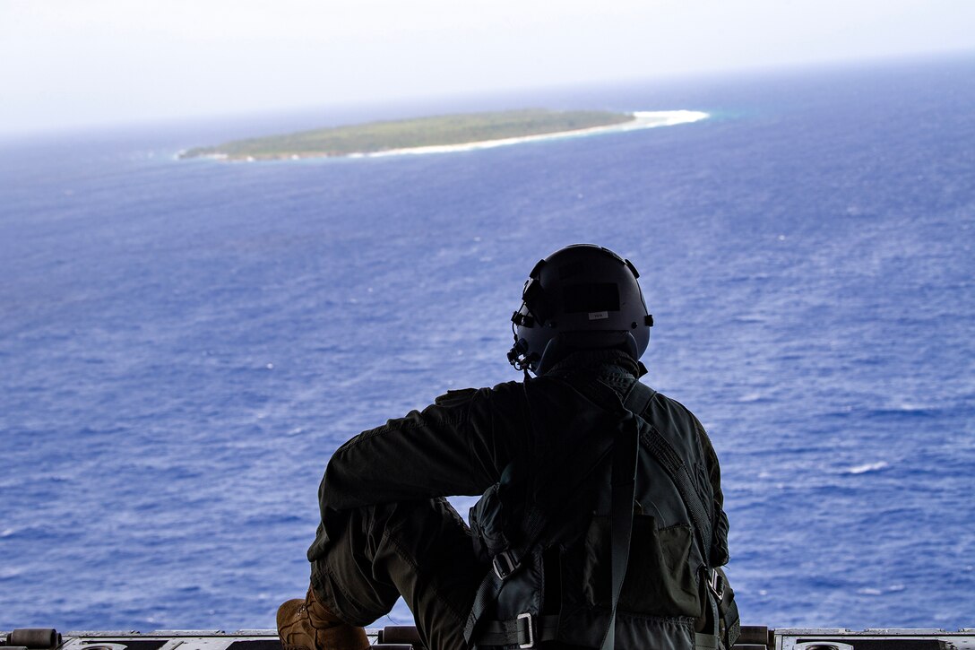 Uniformed person looks over the water from the rear of a C-130J Super Hercules.