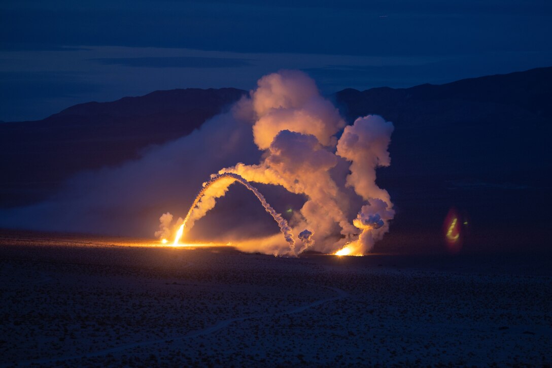 White smoke billows up from a field, against a dark blue sky.
