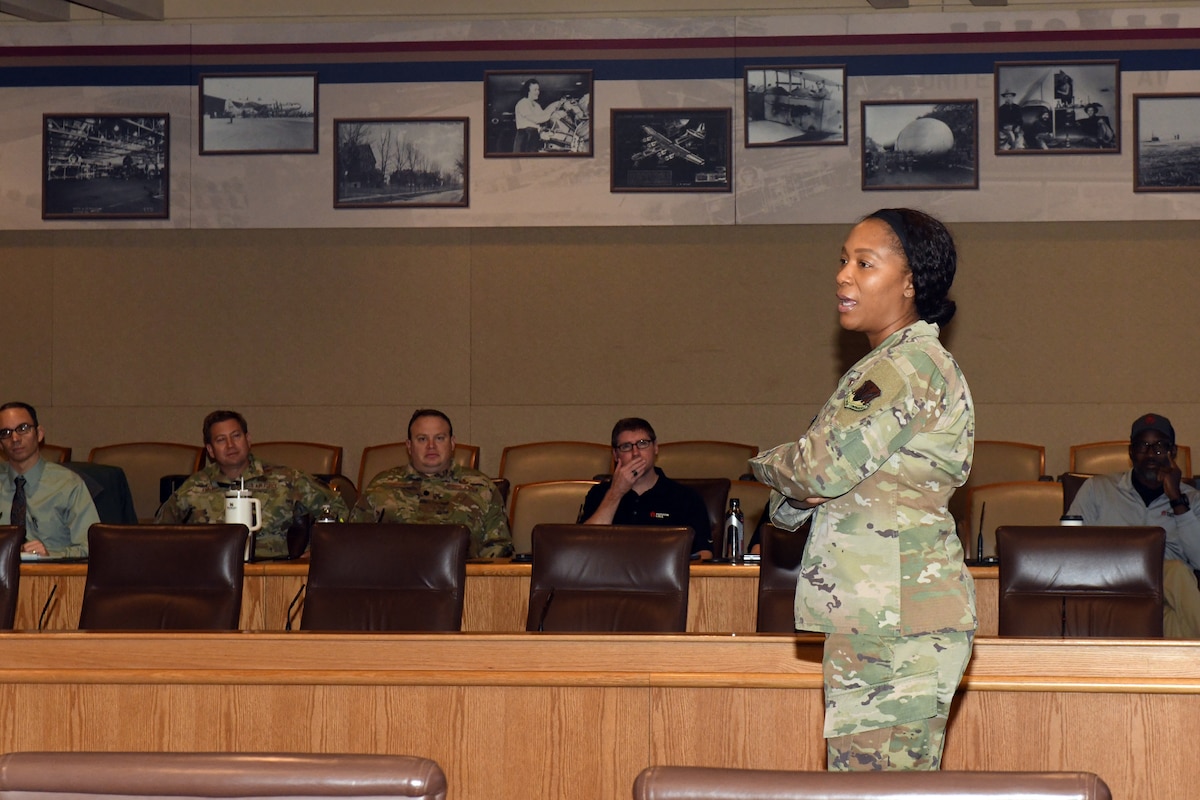 Woman in camouflage uniform stands in front of audience while speaking