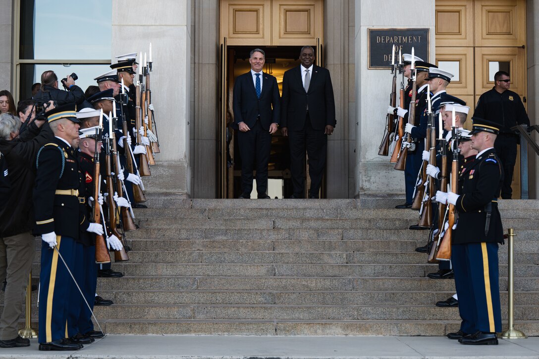 Two men stand at the top of steps in front of the Pentagon.