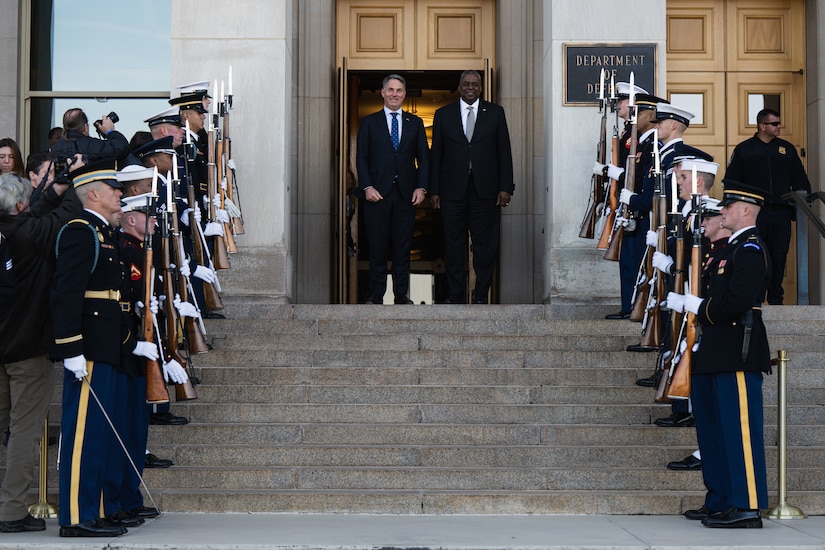 Two men stand at the top of steps in front of the Pentagon.