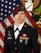 Female Soldier in dress uniform standing in front of two flags.