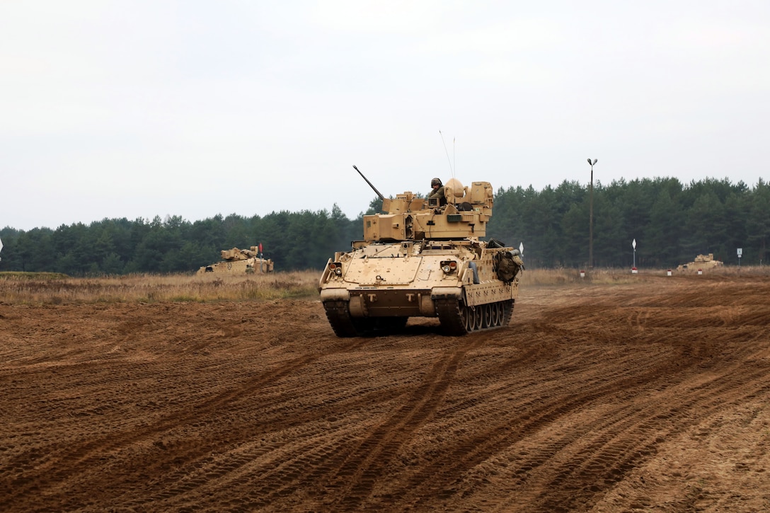 A soldier sits in a tank while driving in an open area.