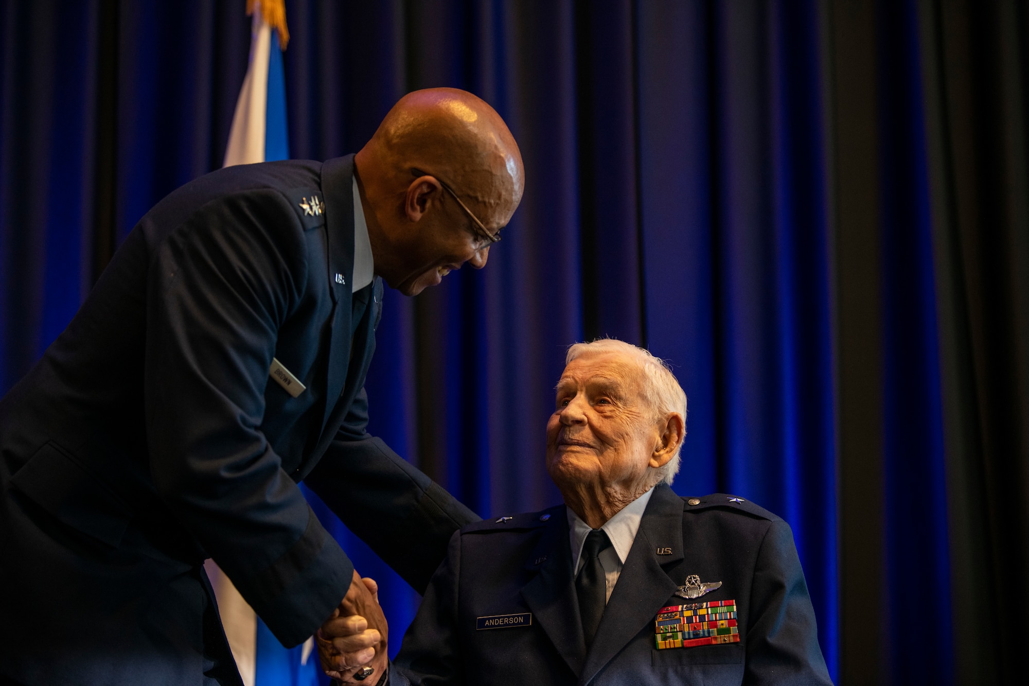 A high-ranking military leader shakes the hand of an elderly man in uniform.