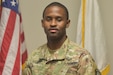 Soldier in uniform standing in front of flag.